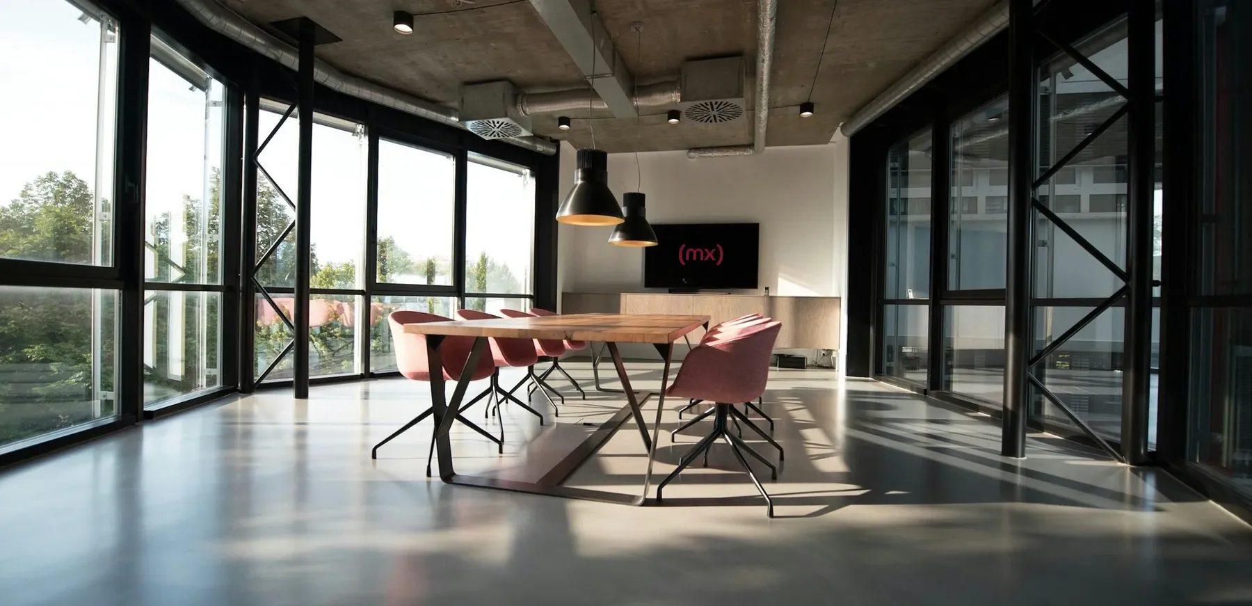 The mx.works studio: a long wood table with pink chairs and the (mx) mark on screen